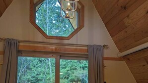 A wooden cabin with a large sliding glass door leading to a deck, a small skylight, and a hanging light fixture. - Golden rings cabin on Homestead W/Hot Tub (qathet Regional District)