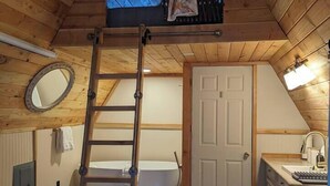 A wooden interior with a bathtub, a ladder, a door, and a small kitchenette. - Golden rings cabin on Homestead W/Hot Tub (qathet Regional District)