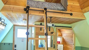 Un dormitorio acogedor en el ático con una cama de altillo, una escalera de madera y un sofá verde.
