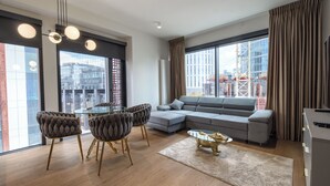 A modern living room with a glass dining table, cushioned chairs, a grey sectional sofa, and a decorative glass coffee table. - Towarowa Towers (Warsaw)