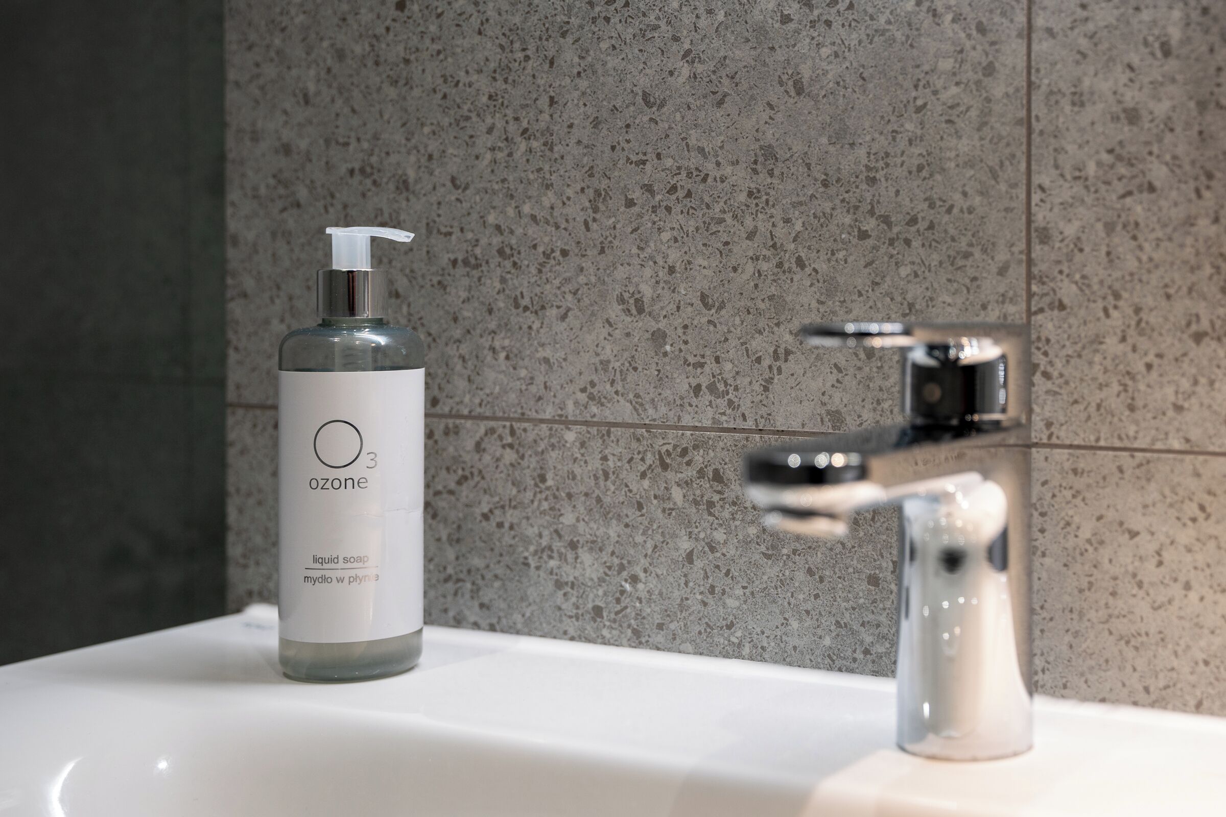 A bathroom with a white sink, a bottle of liquid soap, and a faucet.