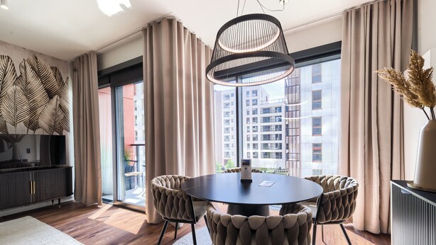 A modern dining area with a round table, cushioned chairs, and a pendant light. - Towarowa Towers (Warsaw)