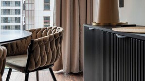 A modern living room with a round table, a tufted chair, a dark-toned cabinet, and a large lamp. - Towarowa Towers (Warsaw)