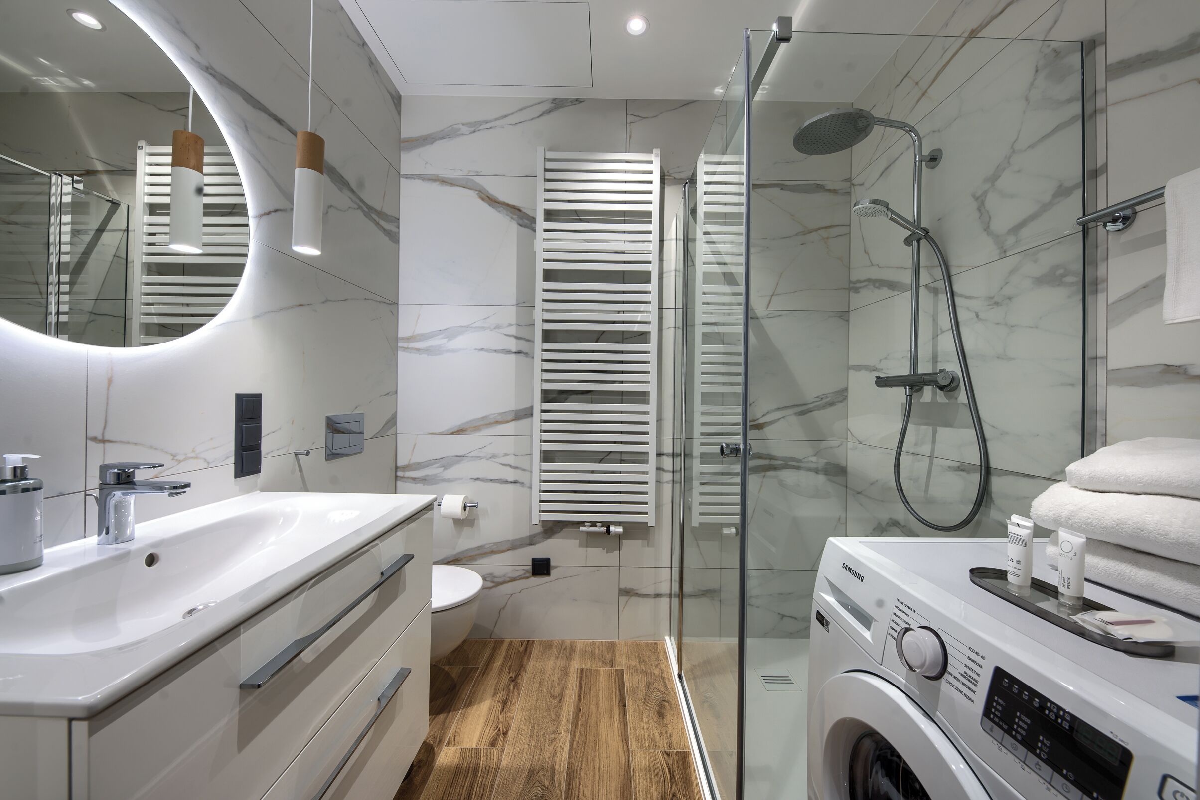 Un baño moderno con pared de mármol, lavamanos, inodoro, cabina de ducha de vidrio y lavadora integrada.