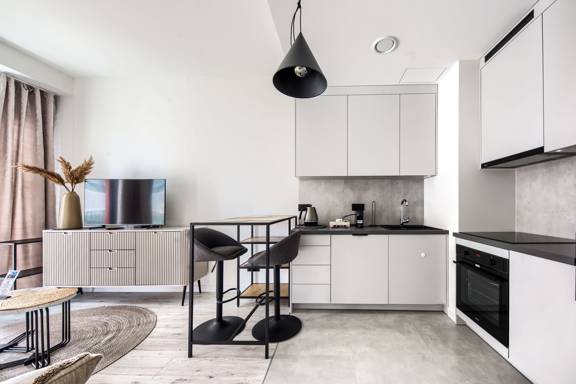 A modern kitchen with white cabinets, a black countertop, and a built-in oven. There is a dining area with a round table and chairs.