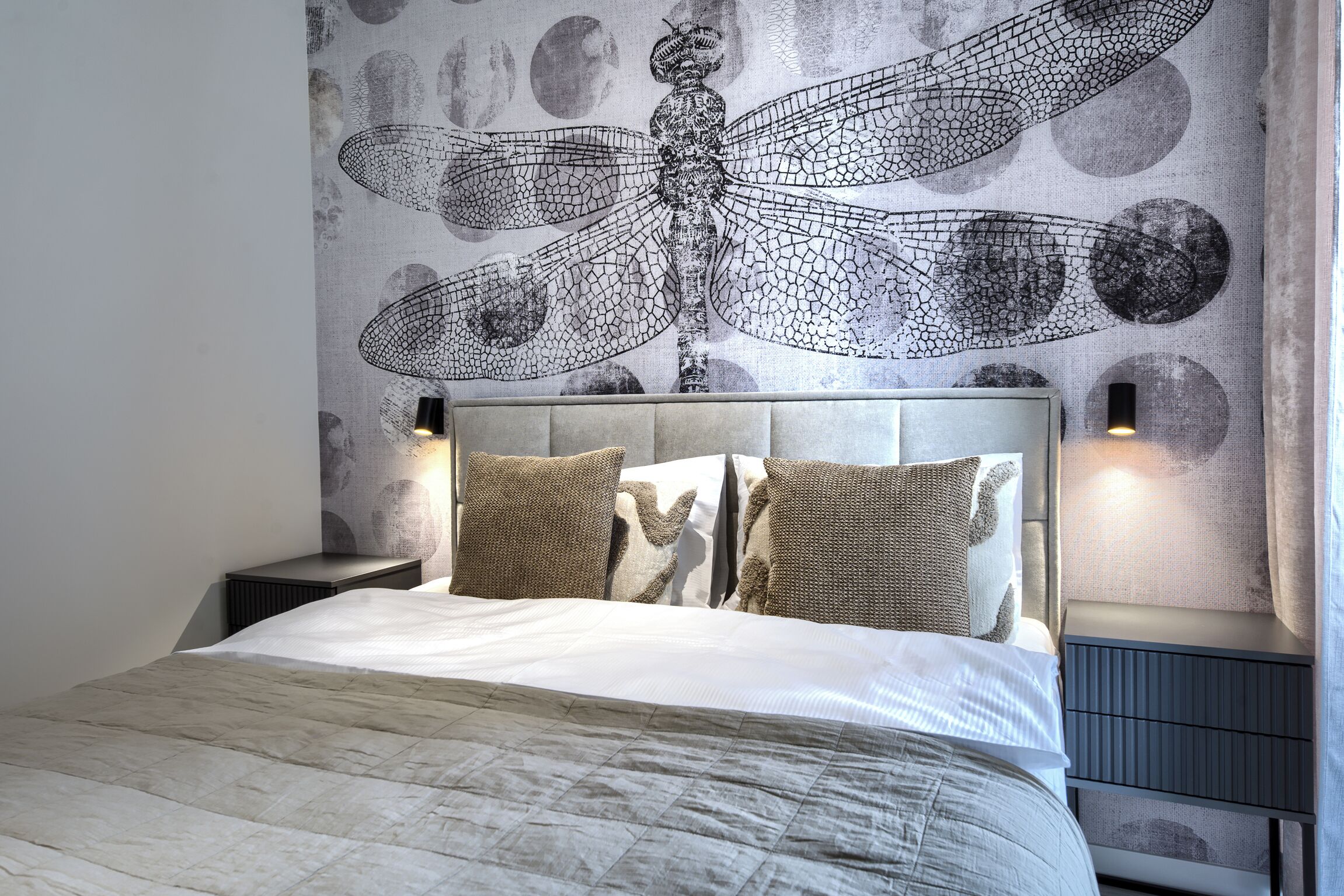 Een slaapkamer met een groot bed, een hoofdbord met een libellenmotief en twee nachtkastjes met lampen.