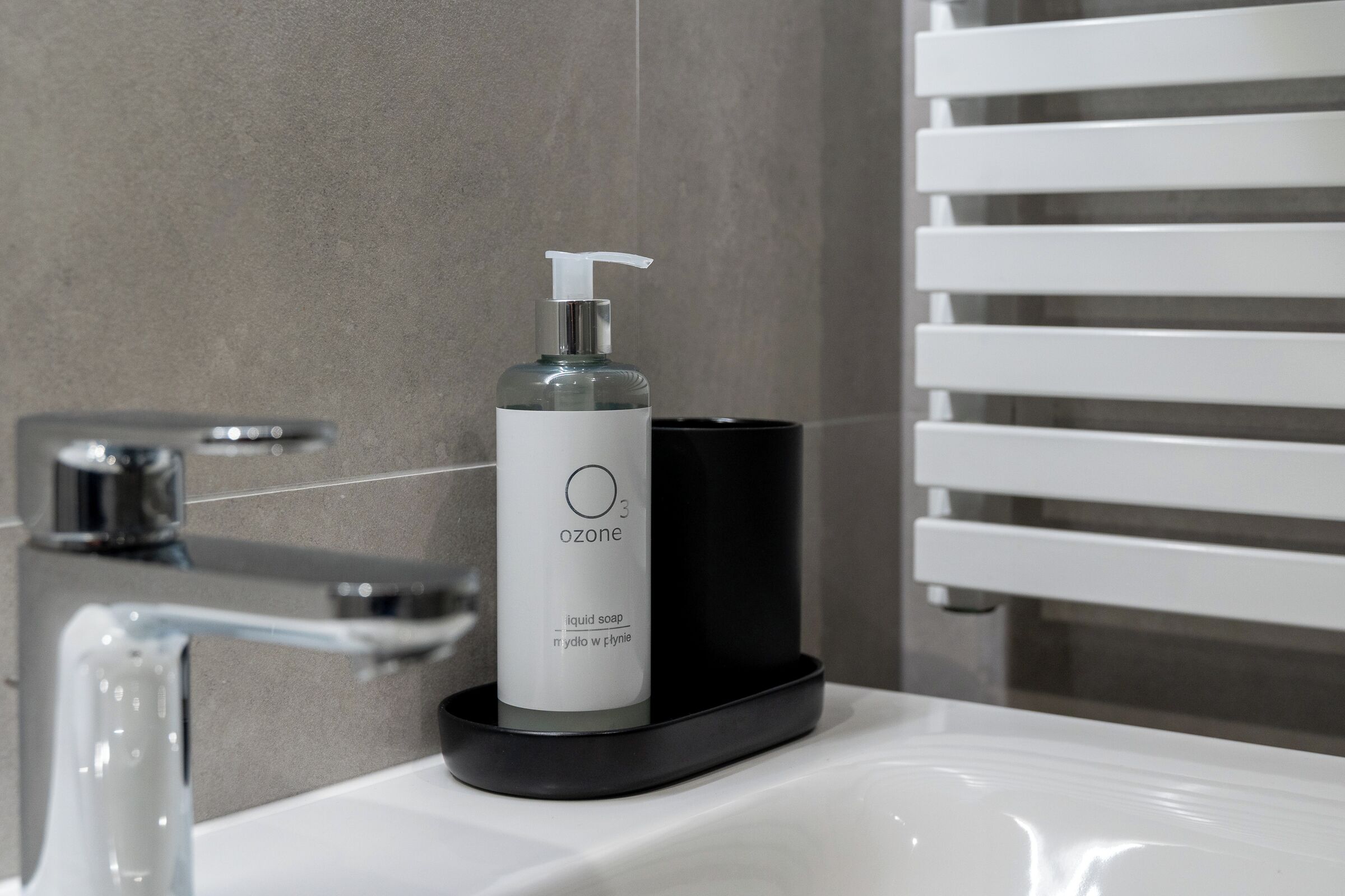 A bathroom with a white sink, a soap dispenser labeled 'ozone', and a black soap holder.