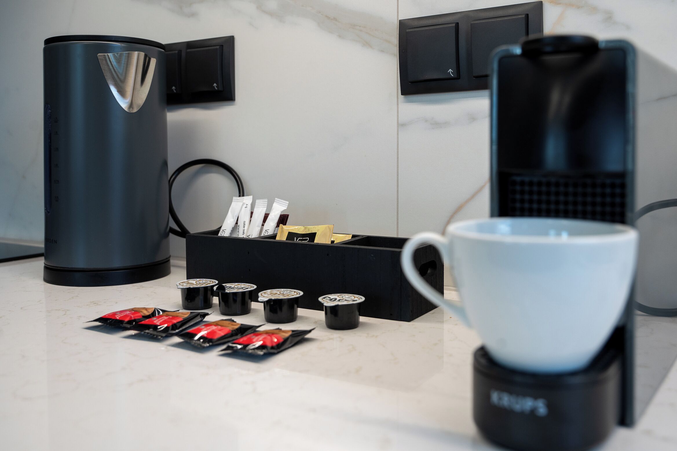 Una cafetera, un dispensador de cápsulas de café y una taza sobre una encimera de cocina.