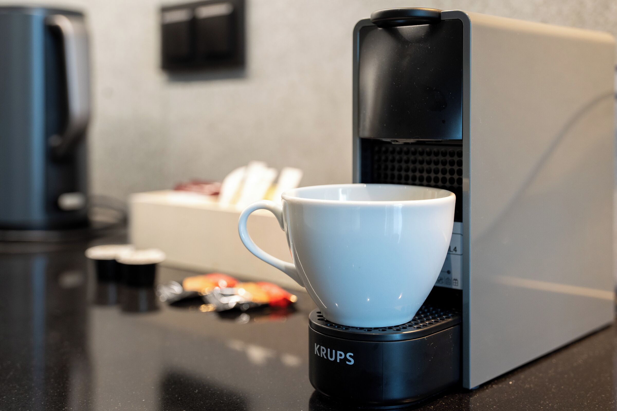 A coffee maker with a cup on its base, a box of tissues, and a bag of snacks on a countertop.