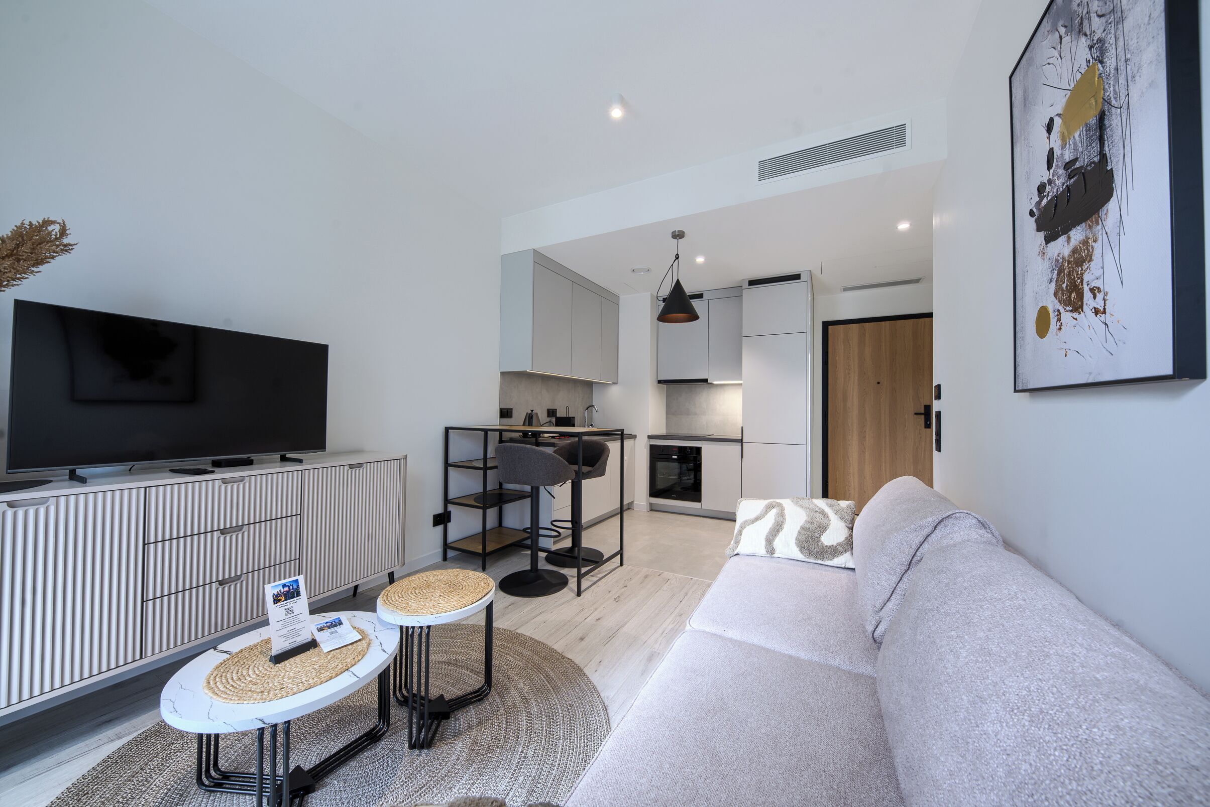 A modern living room with a flat-screen TV, a sofa, a coffee table, and a kitchen area in the background.