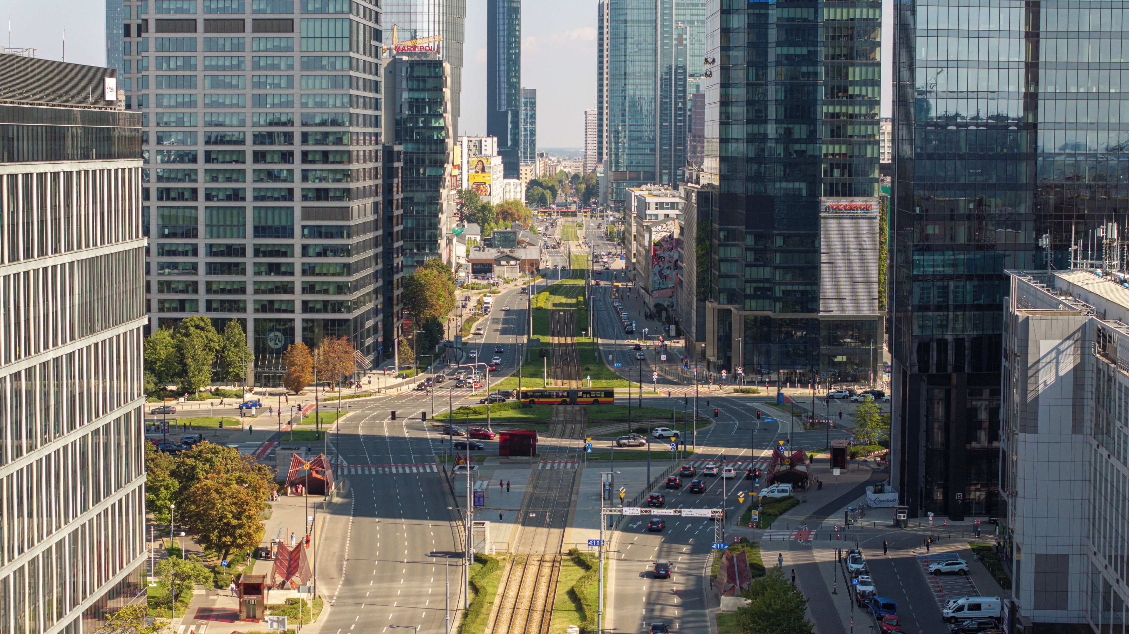 Un paysage urbain avec des immeubles modernes de grande hauteur, un rond-point central et une ligne de tramway.