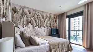 A modern bedroom with a large bed, a headboard with a leaf pattern, a TV, and a view of a building through a large window. - Towarowa Towers (Warsaw)
