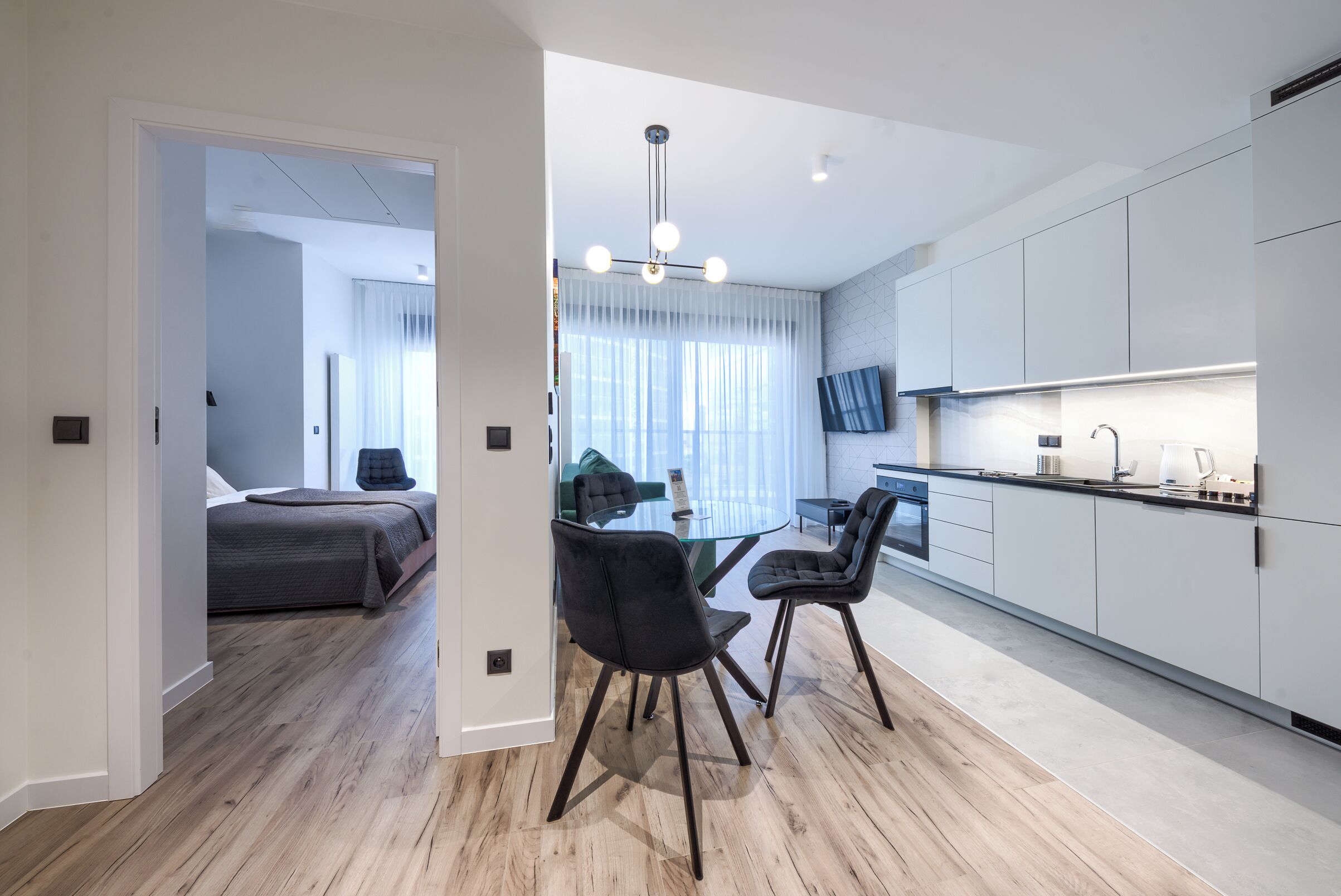 A modern apartment with a dining area, kitchen, and bedroom.