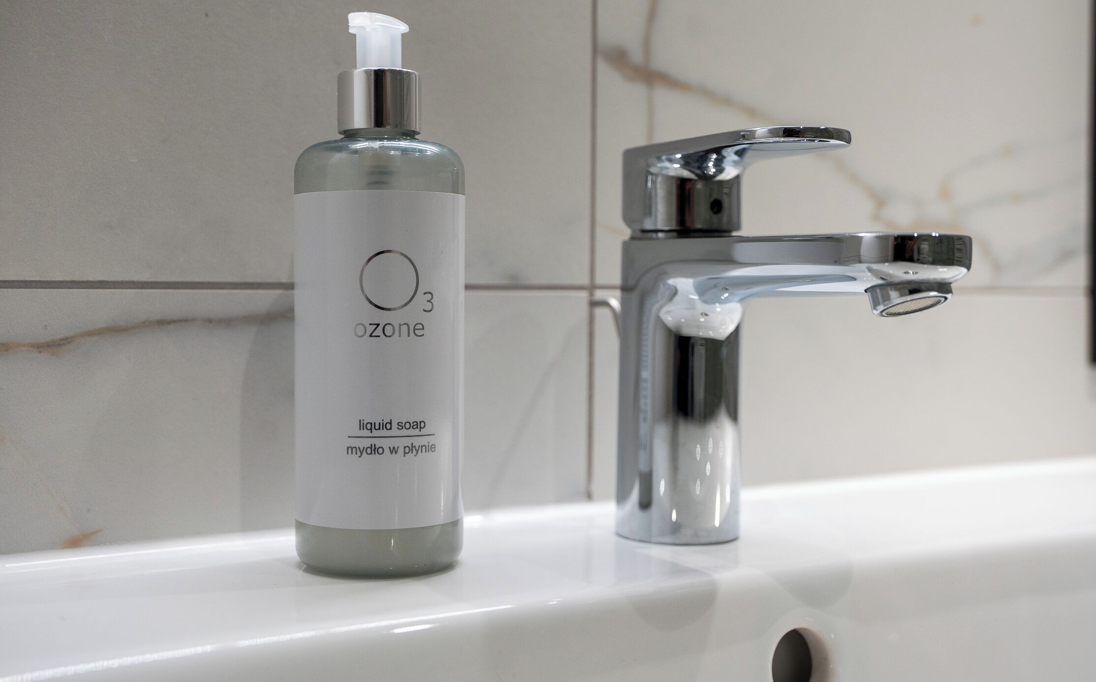 Un lavabo de salle de bain avec un robinet chromé et un flacon de savon liquide étiqueté « ozone ».