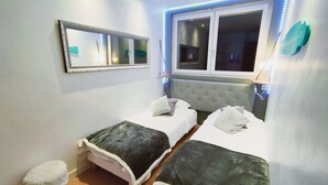 A bedroom with two beds, a small stool, a mirror, and a window with blinds. - Balneo 100m beach (Berck)