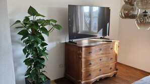 A living room with a flat-screen TV, wooden dresser, and a potted plant.