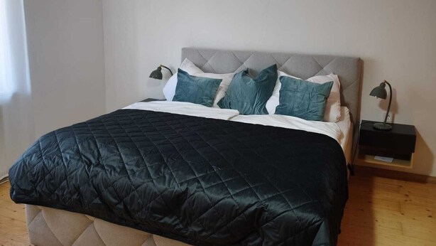 A bedroom with a bed, a nightstand, a lamp, and a hanging light fixture.
