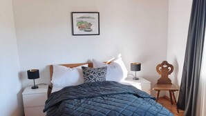 A bedroom with a wooden bed, a nightstand, a bedside table, a hanging lamp, and a framed picture on the wall.