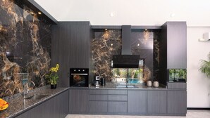 A modern kitchen with dark cabinetry, a built-in oven, and a large window overlooking a pool.