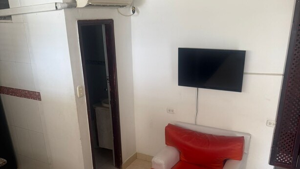 A hotel room with a bed, a red and white chair, a TV mounted on the wall, and an air conditioning unit. - Studio apartment near the 👙👙🏖️ wing (Santa Marta)
