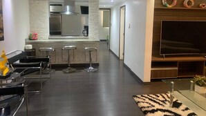 A modern kitchen with a central island, bar stools, and a flat-screen TV on a wooden wall.