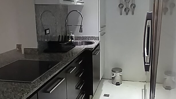 A modern kitchen with dark cabinets, a stainless steel refrigerator, and a marble countertop.