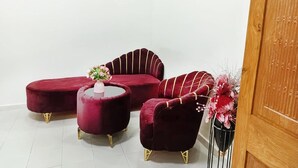 Zona d'seure en cantonada amb un sofà corbat i dos poufs rodons, una porta de fusta i un vas amb flors.