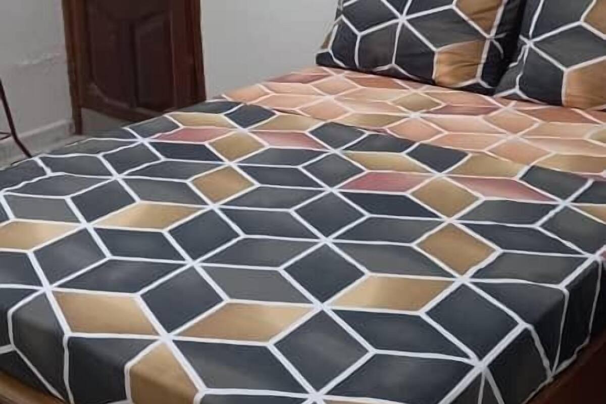 A bed with a geometric patterned bedspread, a wooden headboard, and a wooden door in the background.