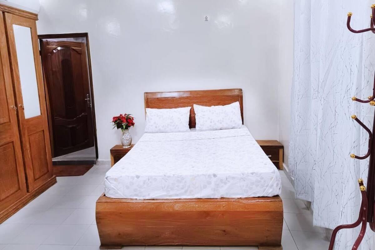 A bedroom with a wooden bed, white curtains, and a wooden wardrobe.
