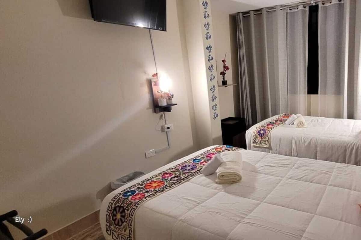 Habitación de hotel con dos camas, un televisor montado en la pared y una ventana con cortinas.