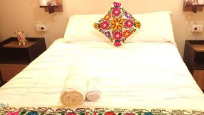 A neatly made bed with a decorative pillow, two bedside tables with figurines, and a patterned bedspread. - Oasis Inka Machupicchu (Aguas Calientes)