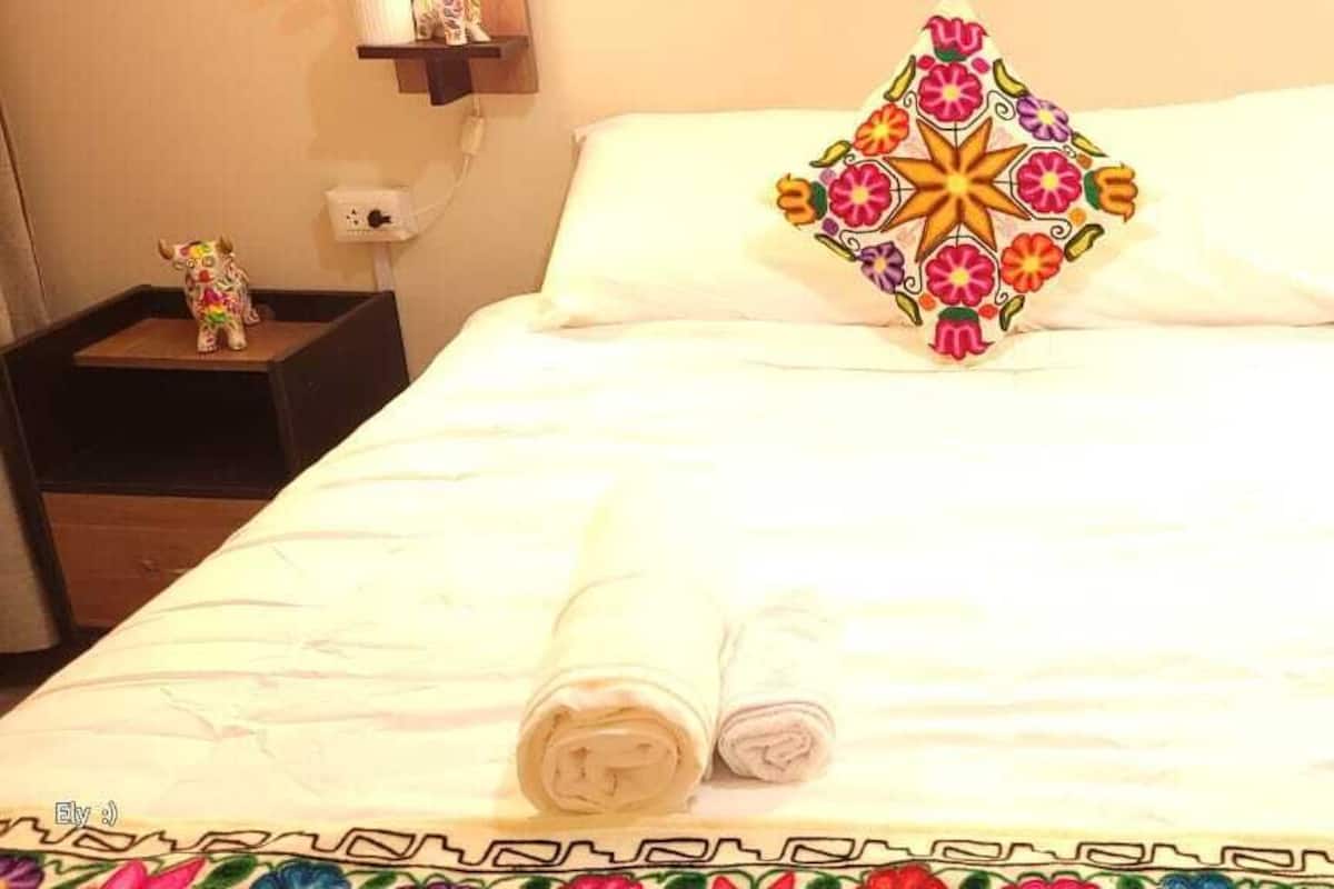 Una cama bien hecha con un cojín decorativo, dos mesitas de noche con figuritas y una colcha estampada.