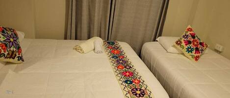 Een hotelkamer met twee bedden, elk voorzien van een kleurrijk geborduurd kussen en een netjes opgevouwen handdoek.