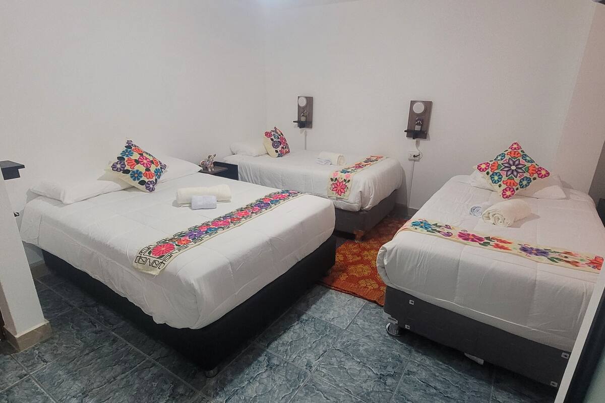 Habitación de hotel con tres camas individuales, cada una con una colcha y almohadas estampadas con motivos florales.