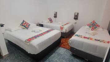 A hotel room with three single beds, each with a colorful floral bedspread and matching pillows.