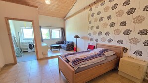 A bedroom with a wooden bed, a nightstand, a sofa, a lamp, and a view of a laundry area.