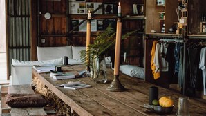 A rustic wooden table with candles, books, and a bowl of fruit. - The K-Tent 2 Summary: (Tintagel)