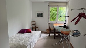 Une chambre à coucher comprenant un lit, une chaise, une planche à repasser et une fenêtre donnant sur un paysage verdoyant.