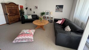 Un salon avec un canapé en cuir noir, une table basse en bois, un divan en cuir noir, un meuble en bois et une bibliothèque avec des photos encadrées.