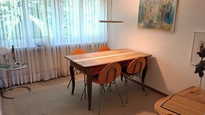 Un coin repas avec une table en bois et quatre chaises, une petite table d’appoint avec une lampe, et un tableau accroché au mur.