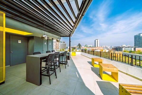 A rooftop terrace with a bar area, seating, and a city view. - Condor 1152 (Santiago)