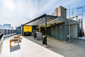 A rooftop terrace with a covered seating area, a small bar, and a yellow accent wall. - Condor 1152 (Santiago)