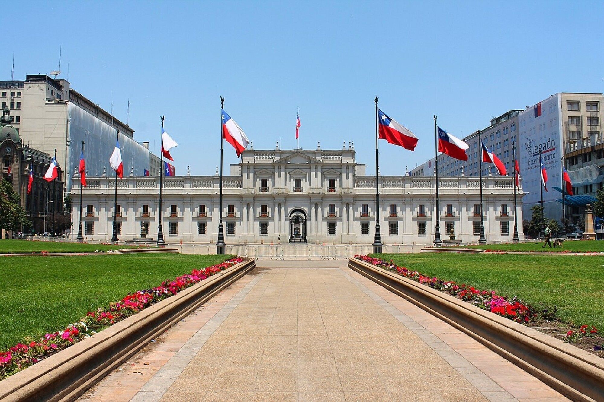 A large, historic building with a central entrance, surrounded by a well-maintained lawn and flower beds.