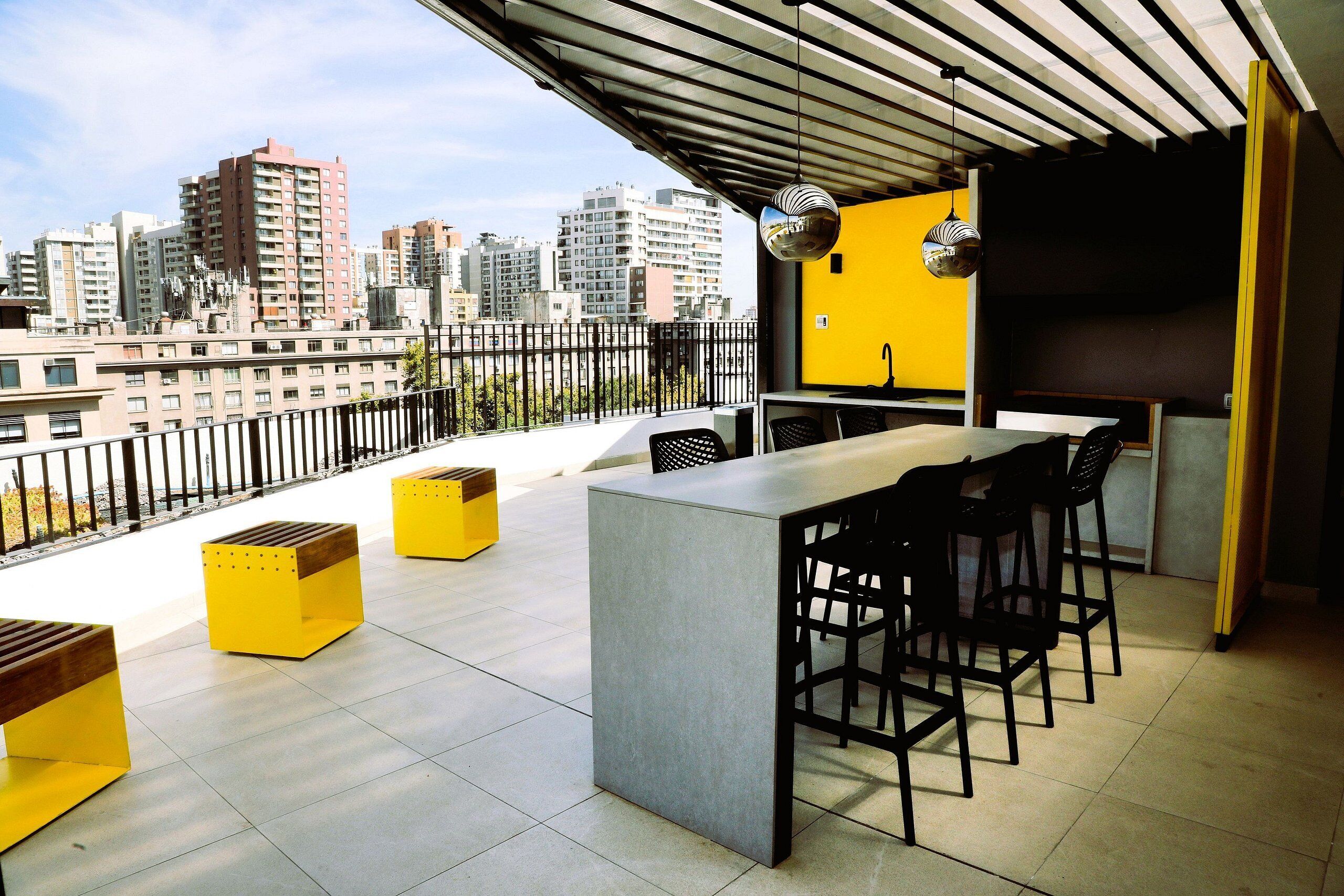 Terraza en la azotea con zona de bar, asientos y vistas a la ciudad.