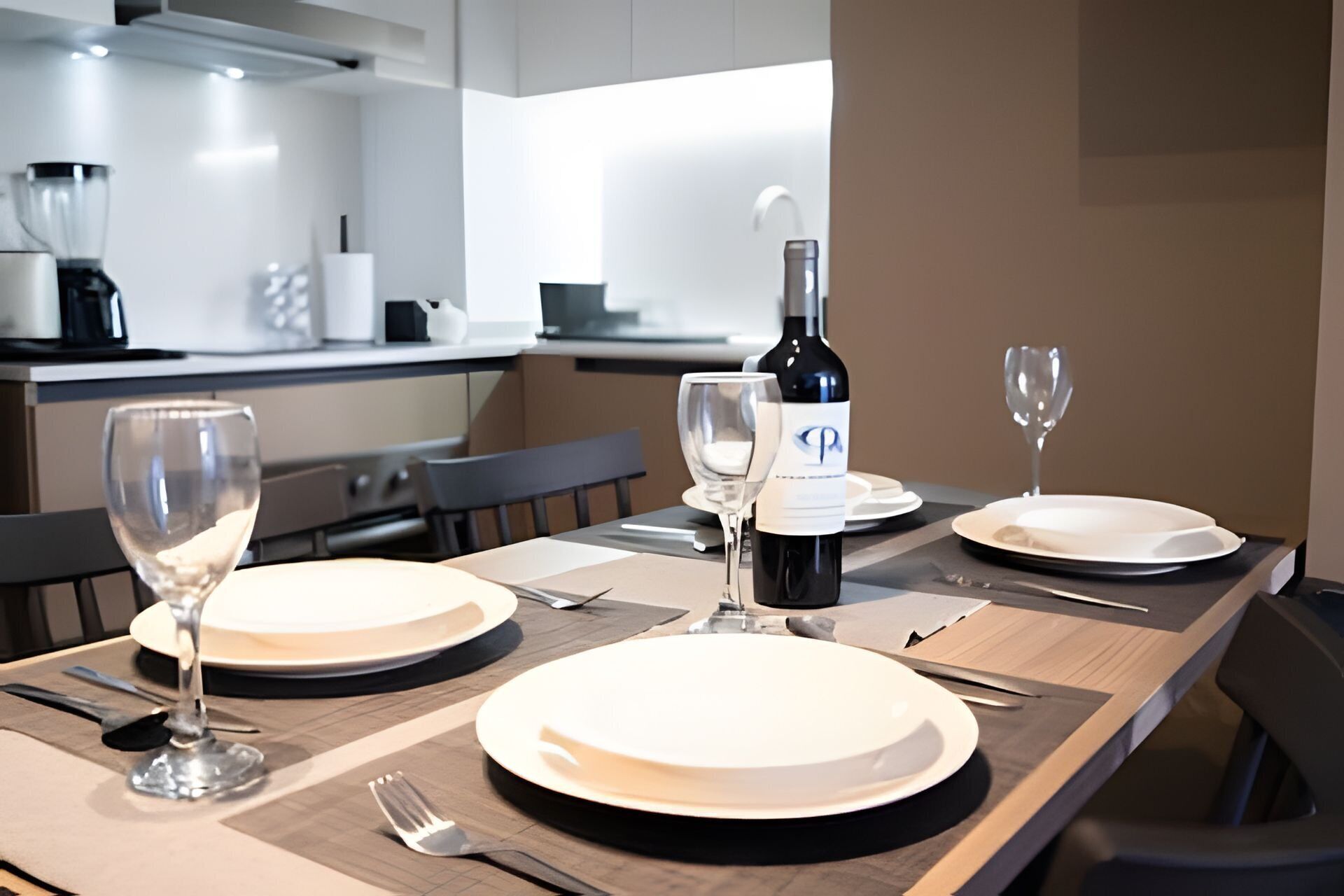 Une table à manger moderne, mise avec de l’assiette blanche, des verres à vin et des couverts. Une bouteille de vin est posée sur la table.