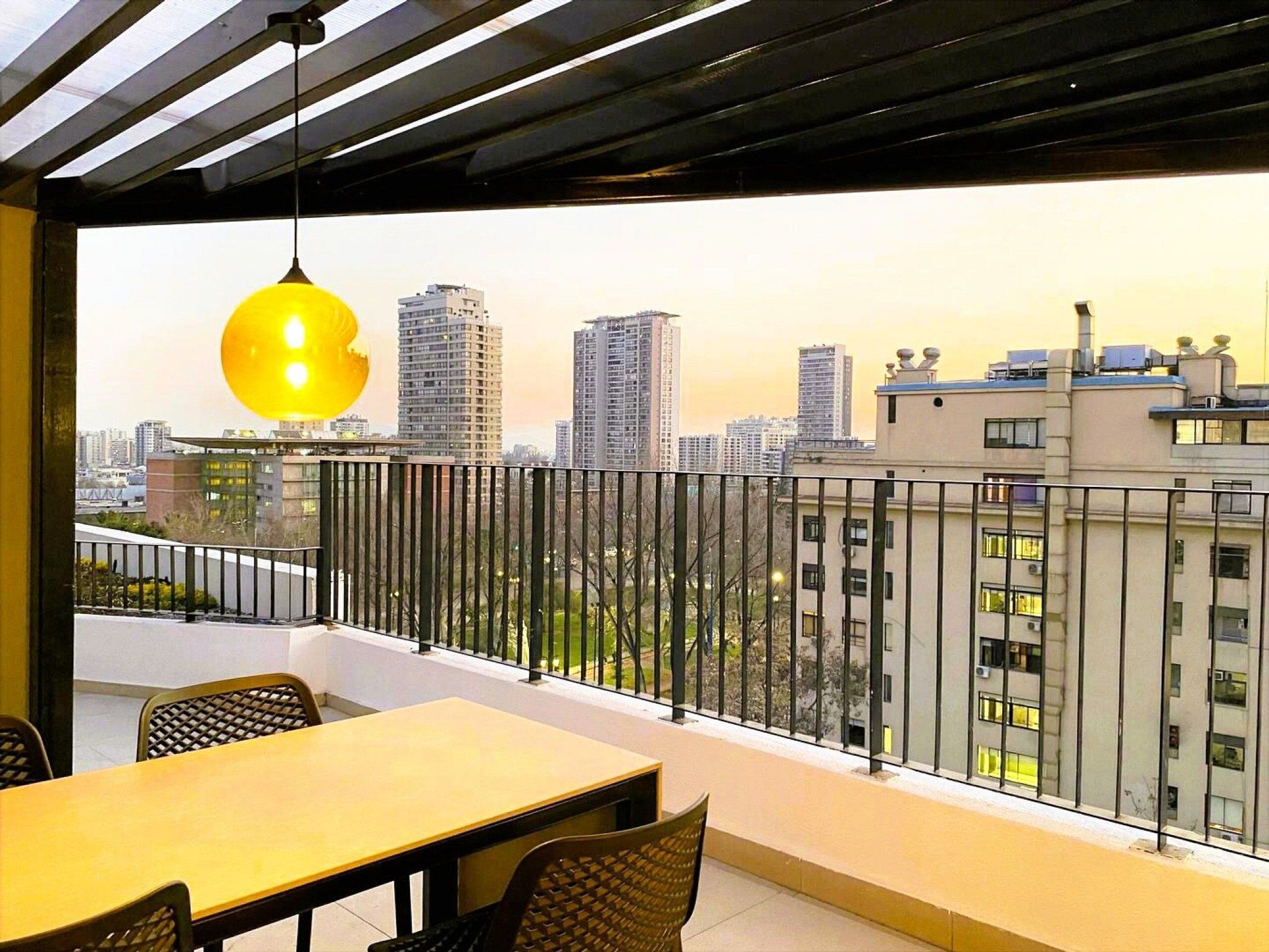Varanda com mesa e cadeiras, luminária pendente e vista panorâmica da cidade.