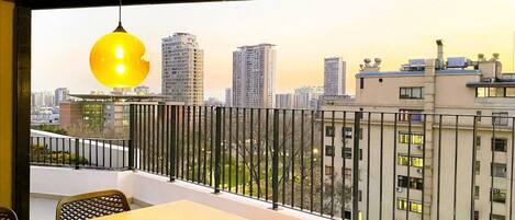 Varanda com mesa e cadeiras, luminária pendente e vista panorâmica da cidade.