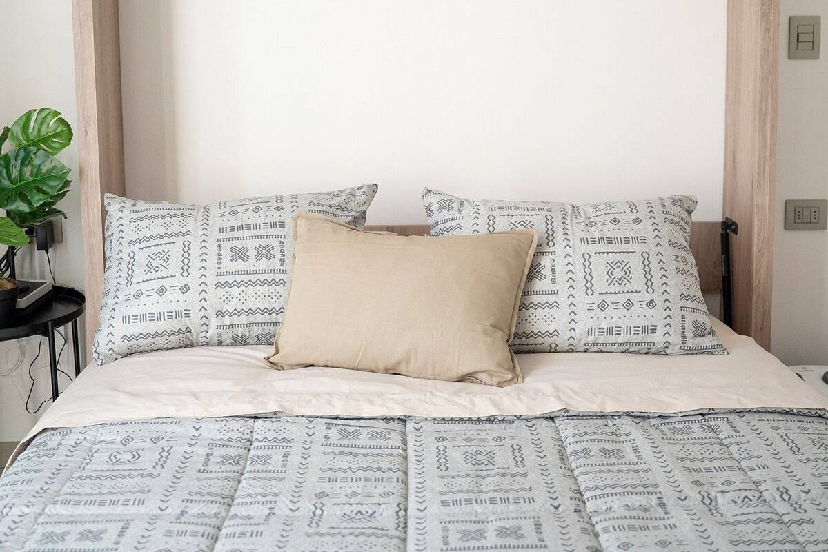 Ein Bett mit gemusterten Bettbezügen, einem Holz-Kopfteil und zwei Kissen mit geometrischem Muster.