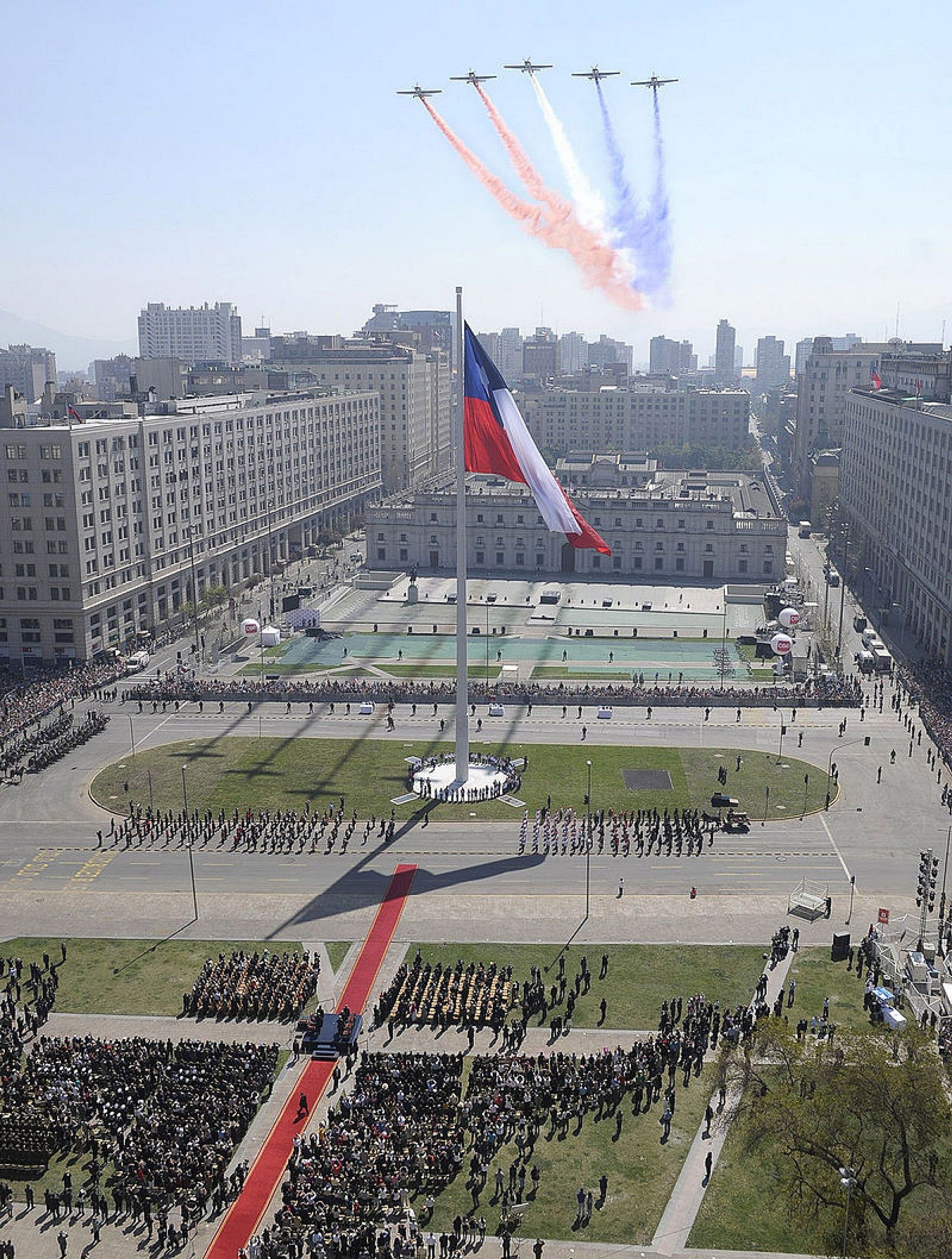 A flagpole with a flag, surrounded by a large crowd and a ceremonial formation.