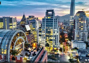 A cityscape with modern high-rise buildings, a distinctive curved glass structure, and a clear view of the surrounding urban area. - Condor 1152 (Santiago)